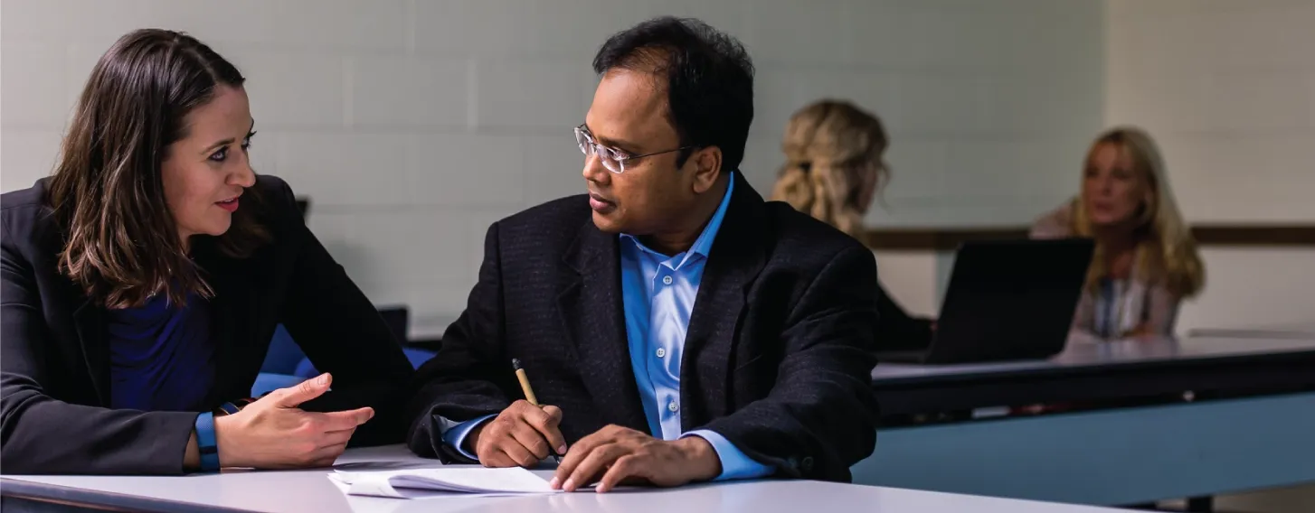 DBA student and professor talking over notes in a classroom.