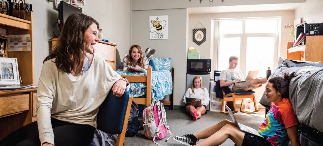 Group of students smiling and chatting in a dorm room.